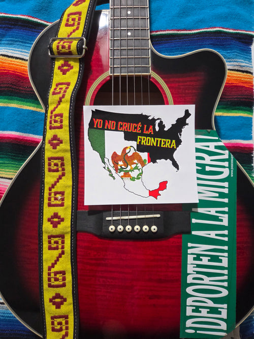 "6" × 6" sticker featuring a close-up of a red acoustic guitar with a yellow patterned Mexican strap, placed on a colorful striped serape blanket. A sticker with a 1848 vintage Mexican flag with text 'YO NO CRUCE LA FRONTERA' is attached to the guitar body, along with a green sign reading 'DEPORTEN A LA MIGRA'.